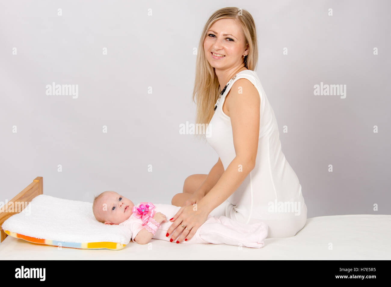 Glückliche Mutter sitzt auf einem Bett in seiner zwei-Monats-Tochter und sieht auf dem Bild Stockfoto
