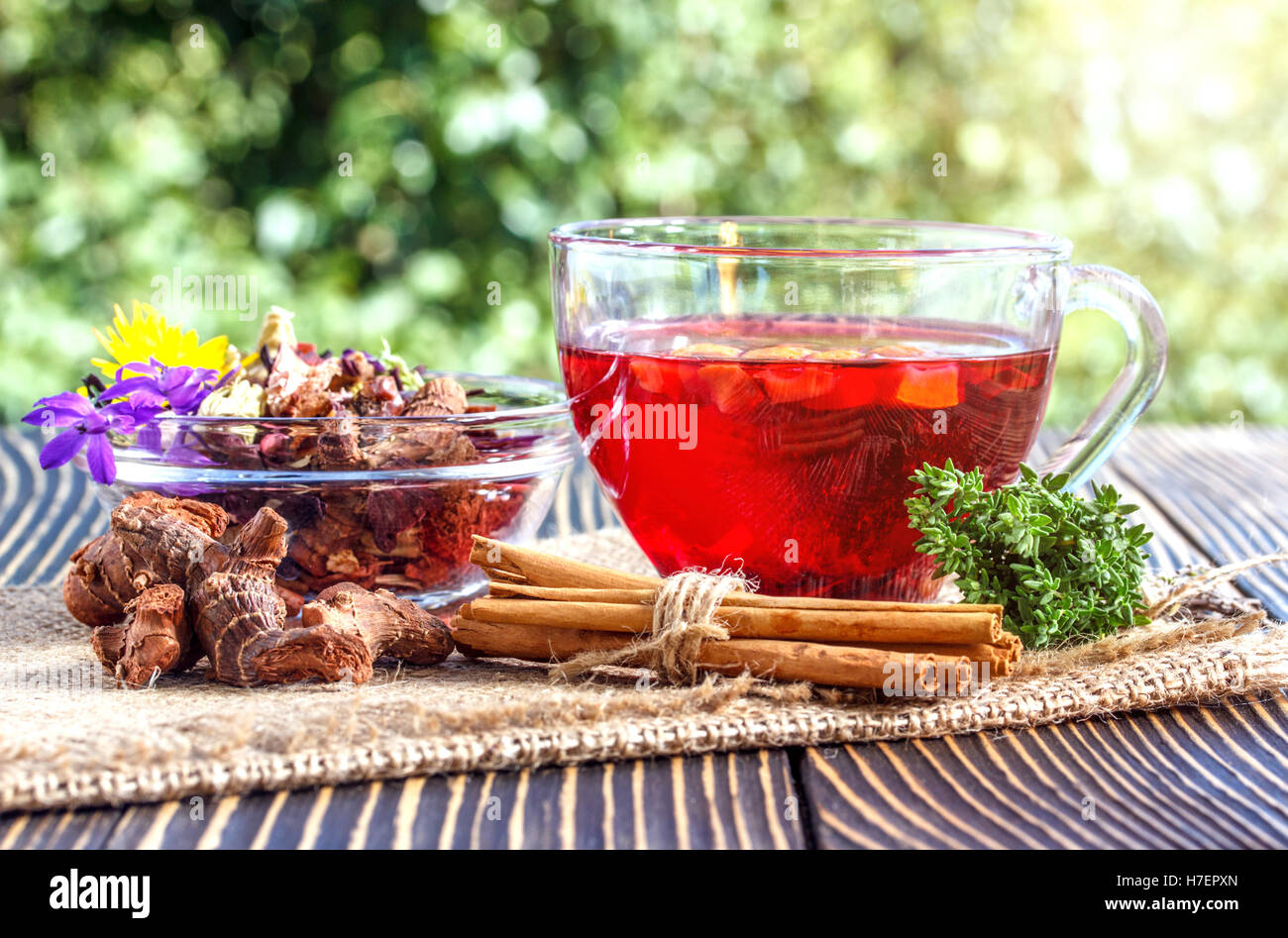 Tasse Tee mit verschiedenen Kräutern und getrockneten Früchten auf einem Holztisch im freien Stockfoto