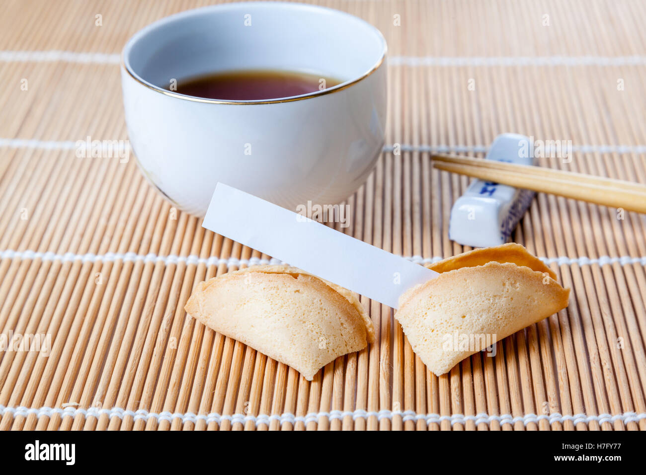 Chinesische Tasse Glückskeks mit leeren Slip auf Bambusmatte mit chinesischen Essstäbchen und Tee eingeritten. Stockfoto