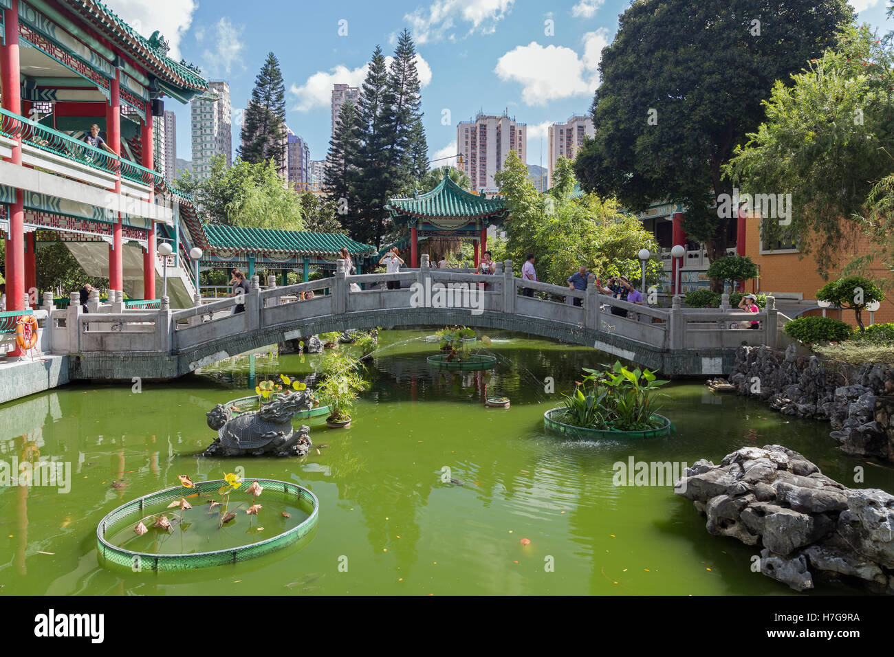 Menschen an einer Brücke neben dem Wasser-Pavillon und einem Teich an der Sik Sik Yuen Wong Tai Sin Temple in Hong Kong, China. Stockfoto