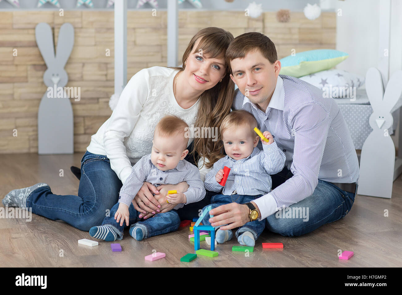 Glückliche junge Familie aus Vater, Mutter und Zwillinge sind aus Holzbohlen Spielzeug Haus gebaut. Stockfoto