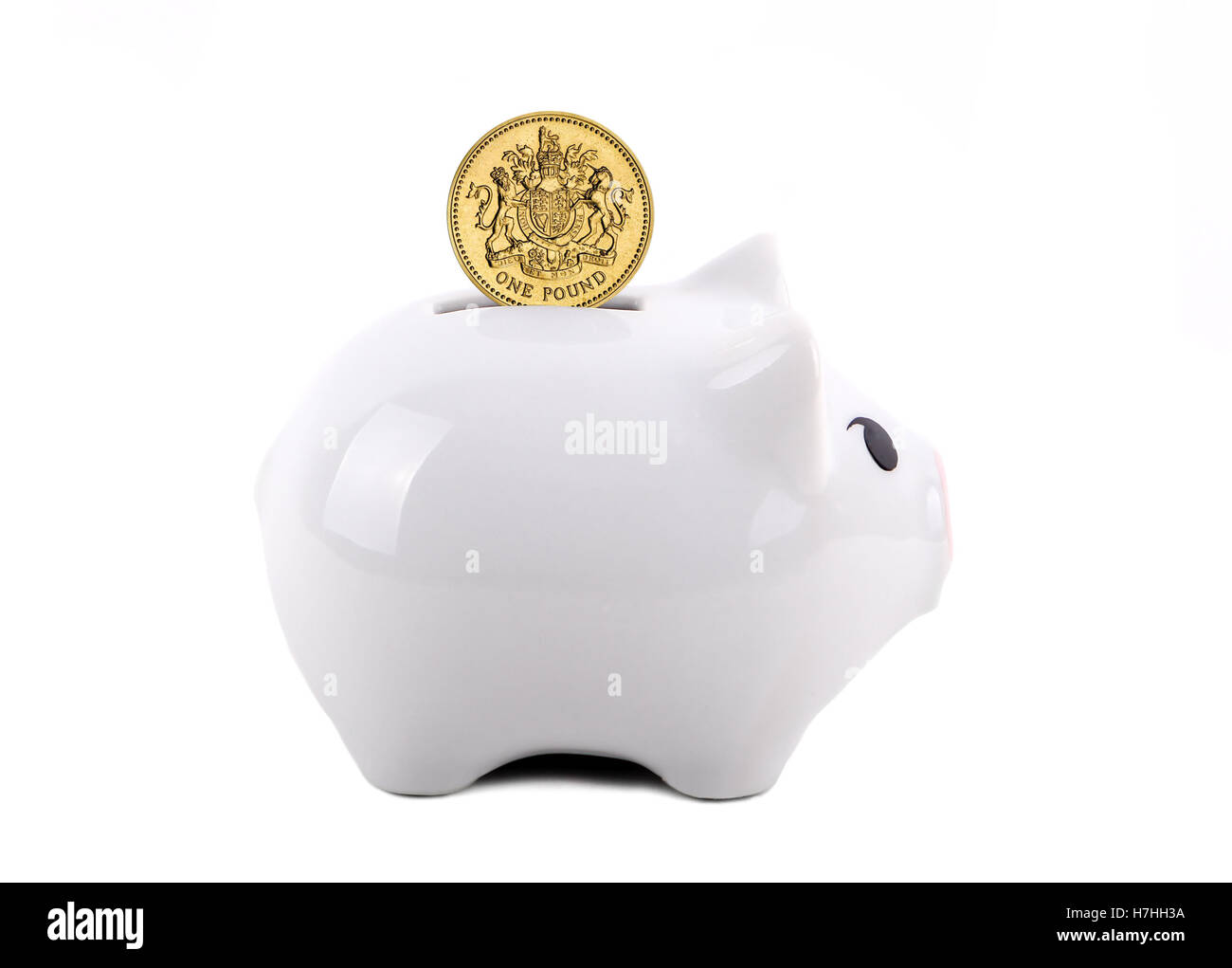 Weiße Sparschwein mit britischen Pfund-Münze in den Schlitz. Idee des Sparens für einen regnerischen Tag, Bildung, Ruhestand. Isoliert auf Stockfoto