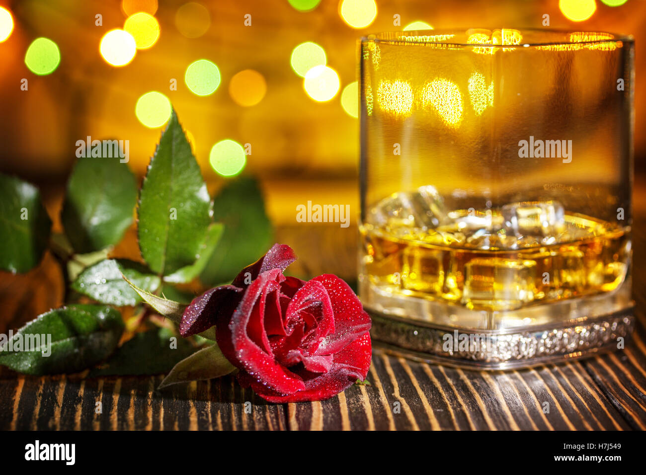 Glas Scotch Whisky und Eis, rote rose im Urlaub bunten Bokeh Hintergrund auf Holztisch Stockfoto