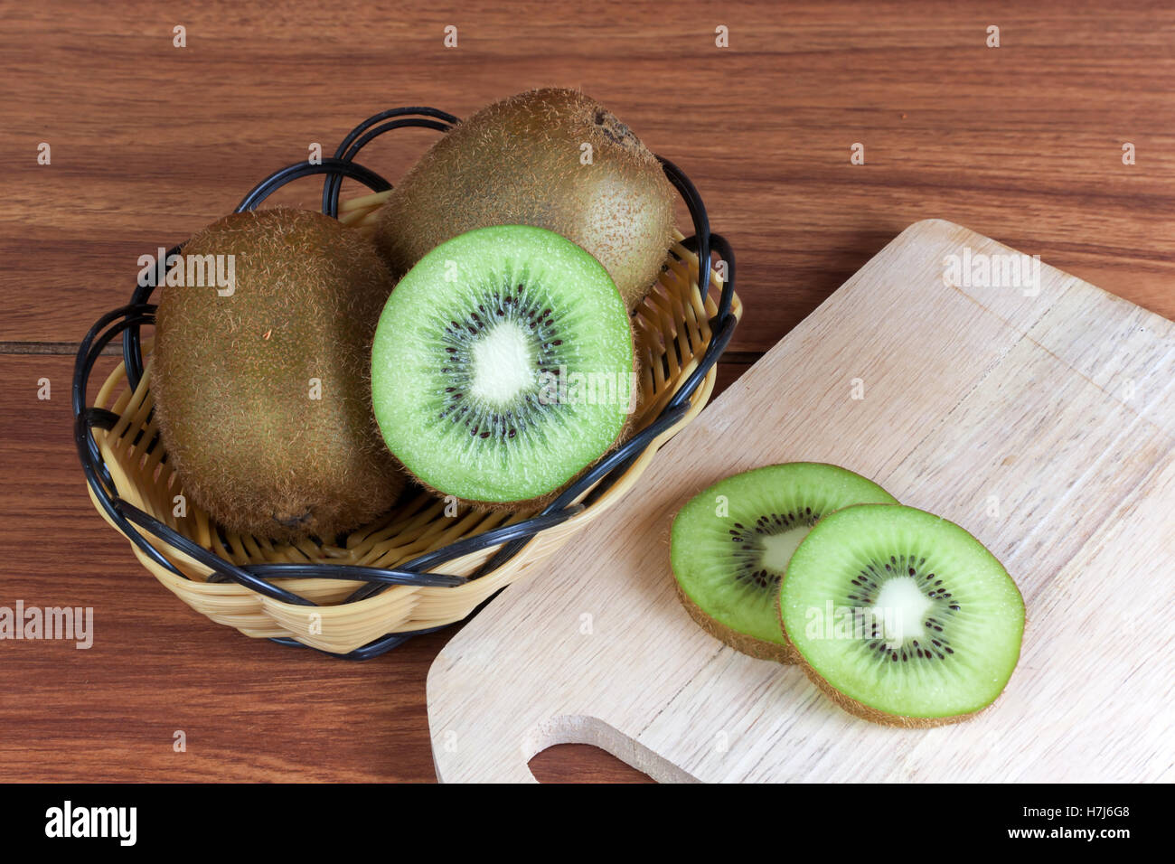 frische Kiwis und Scheiben von Kiwifrucht im Korb auf Holz Stockfoto