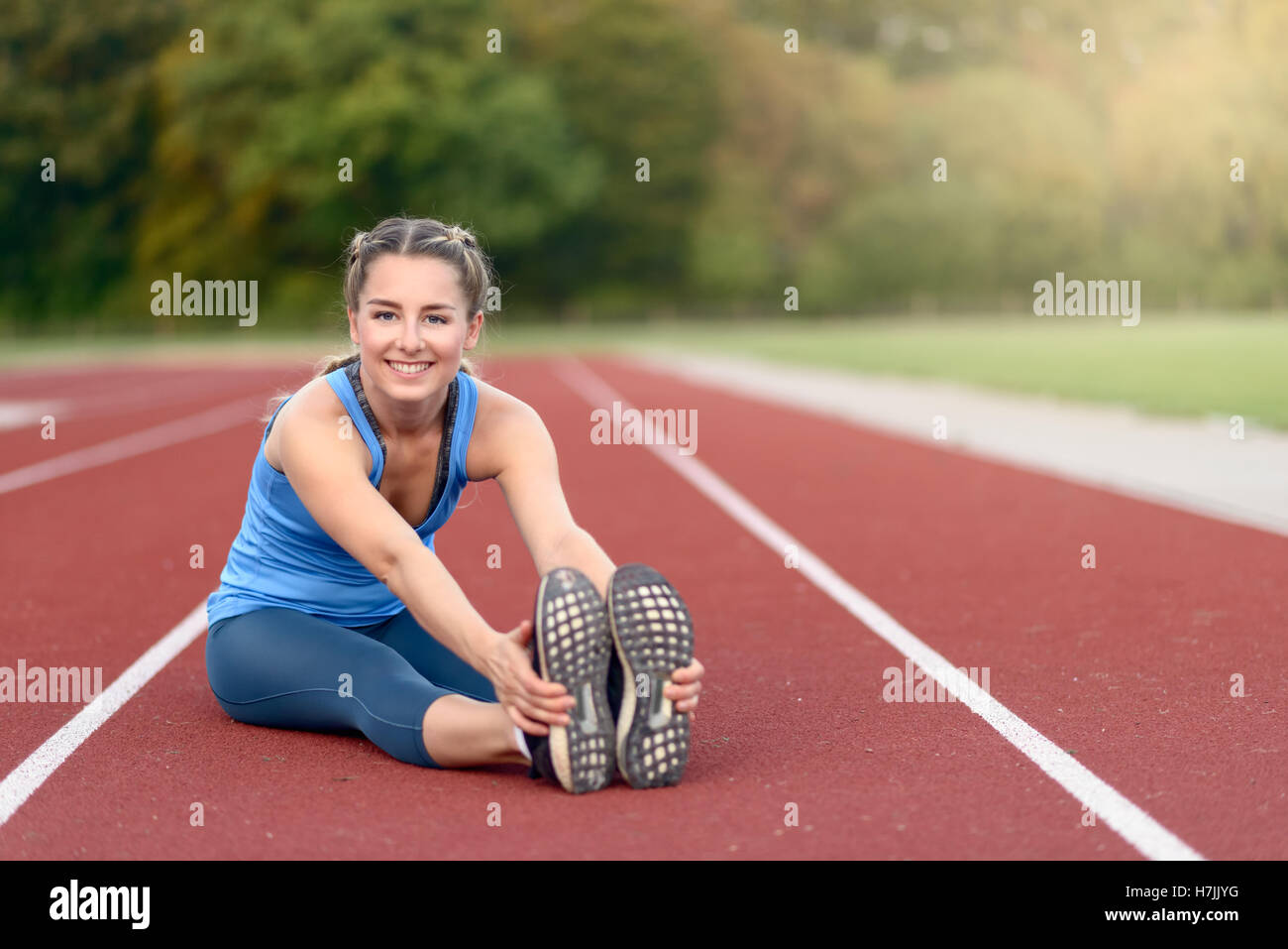 Glücklich Fit junge Frau tun stretching Übungen wie sie sitzt auf einer Leichtathletikbahn Aufwärmen vor dem Training in ein Gesundheits- und f Stockfoto