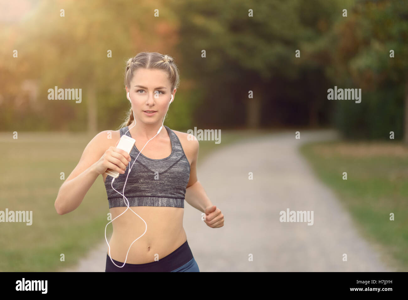 Frau, hören Sie Musik auf ihre Ohrstöpsel und MP3-Player beim Joggen entlang einer Landstraße in einen gesunden Lebensstil-Konzept Stockfoto