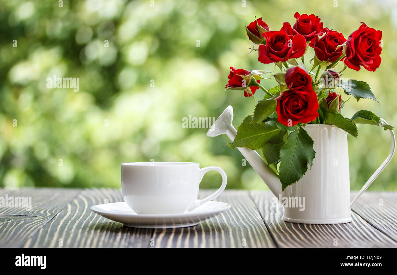 Tasse Kaffee und rote Rosen auf einem Holztisch im Sonnenschein Stockfoto