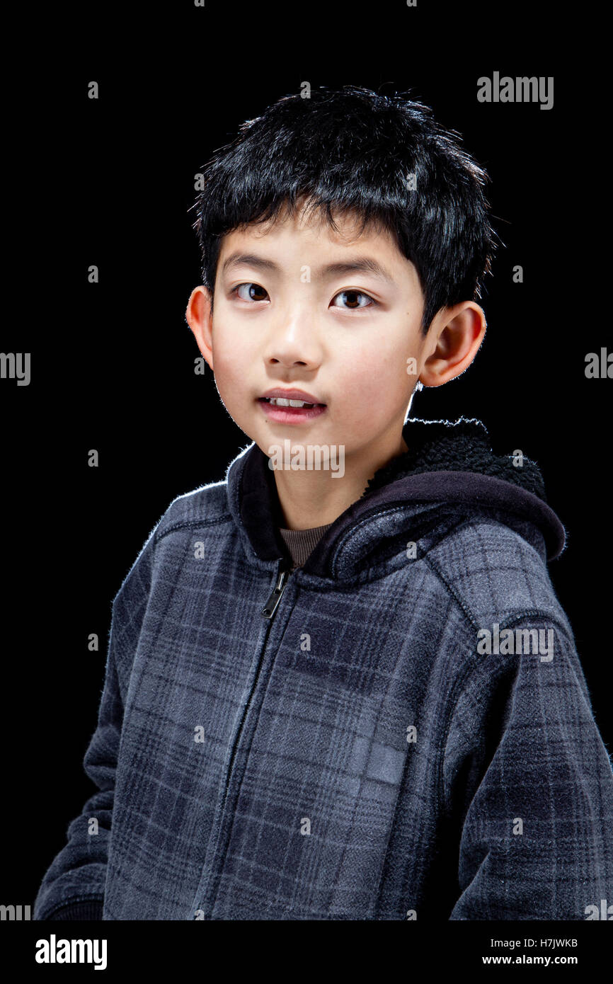 Süße asiatische hübscher Junge posiert im Studio auf schwarzem Hintergrund mit Hintergrundbeleuchtung Wirkung. Stockfoto