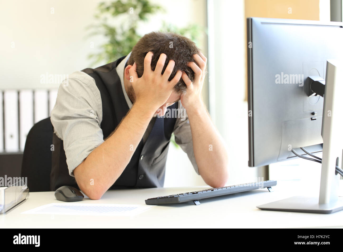 Deprimiert Geschäftsmann nach dem Konkurs klagend mit Händen auf dem Kopf in einem Desktop-PC im Büro Stockfoto