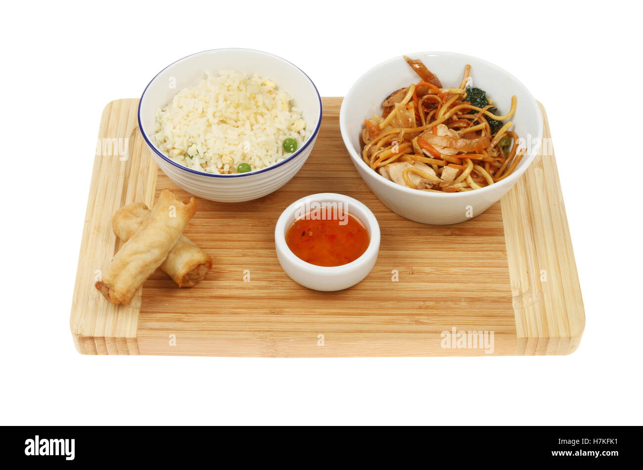 Chinesisches Essen, Reis, Huhn Chow Mein und Frühlingsrollen auf einem Bambus Schneidbrett isoliert gegen weiß Stockfoto