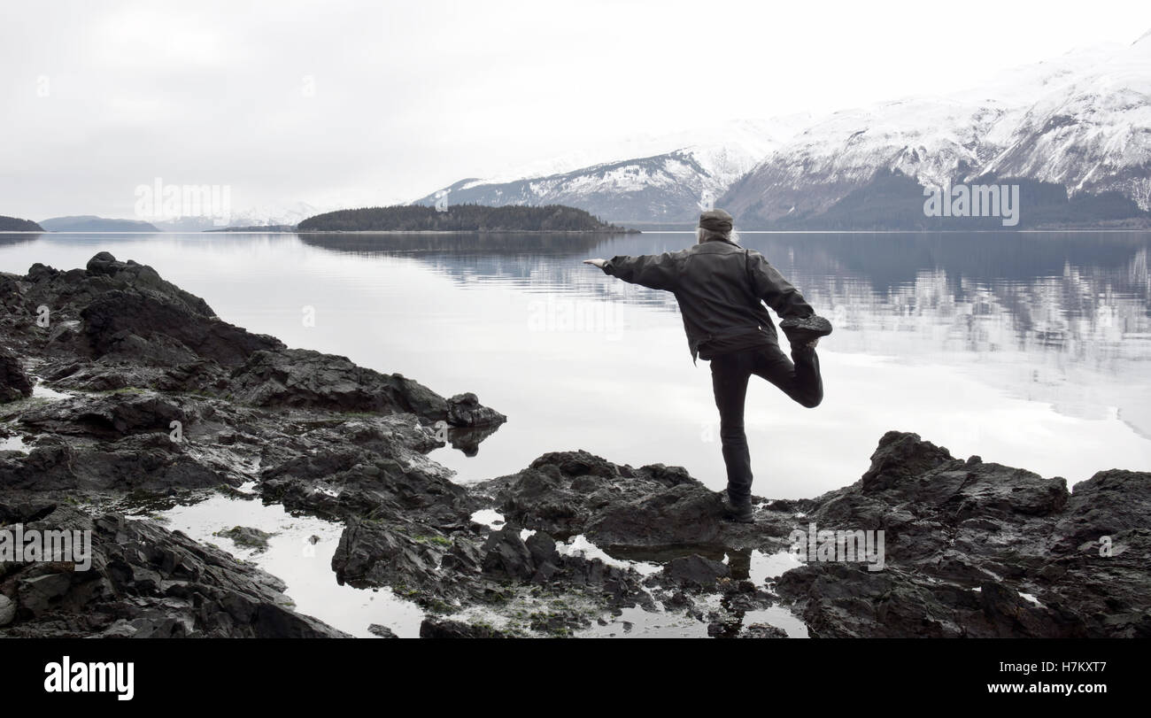 Mann tut eine dumme Yoga stellen an einem steinigen Strand in Southeast Alaska mit gedämpften Farbtöne verarbeitet. Stockfoto