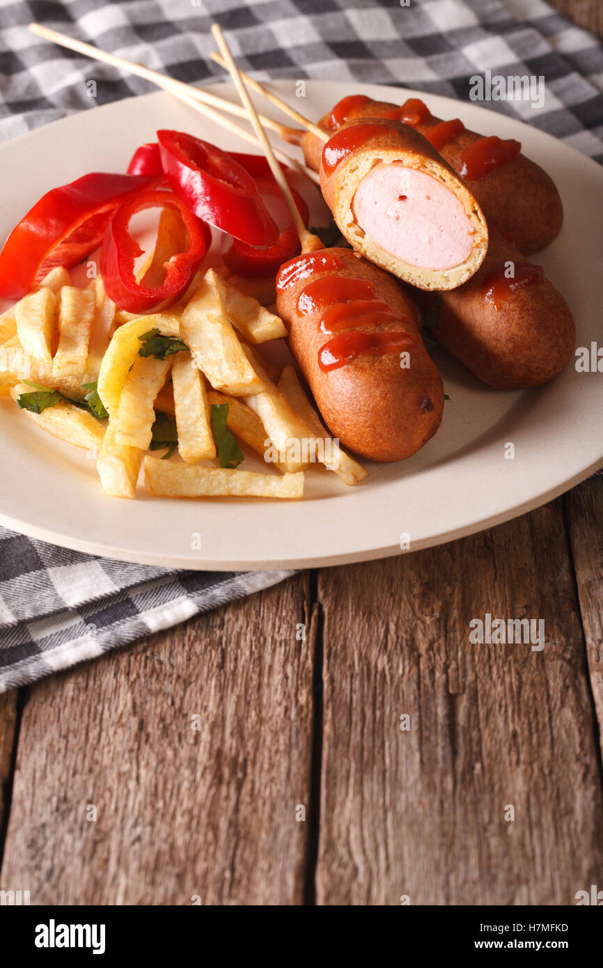 Corndog mit Pommes Frites und Gemüse auf einer Platte Nahaufnahme auf dem Tisch. vertikale Stockfoto