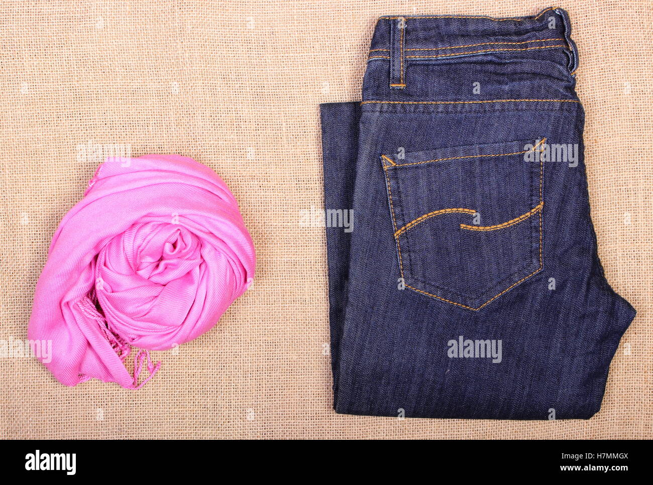 Hosen Jeans und Schal oder Tuch auf Jute Sackleinen Hintergrund, Zubehör, Bekleidung für Frau Stockfoto