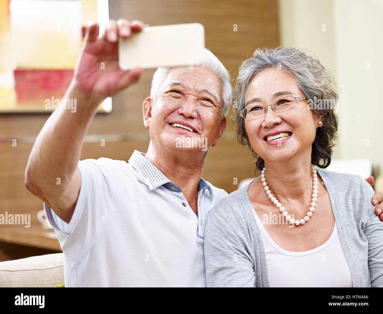 hochrangige asiatische paar die ein Selbstporträt zu Hause mittels Handy Stockfoto