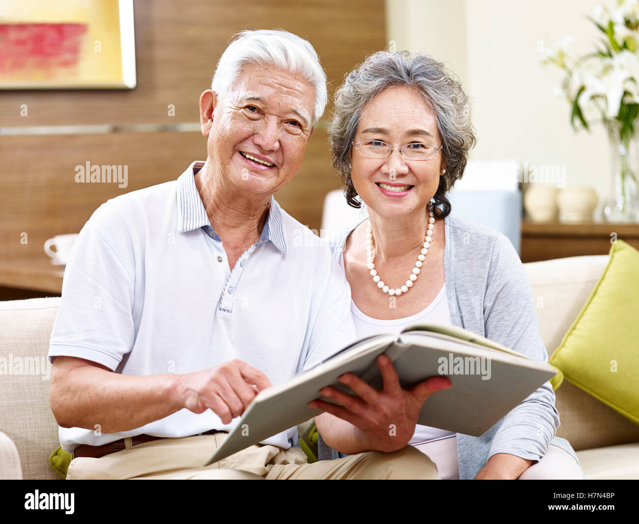 hochrangige asiatische paar auf Couch, einen Blick auf die Kamera zu Lächeln Buch hält Stockfoto