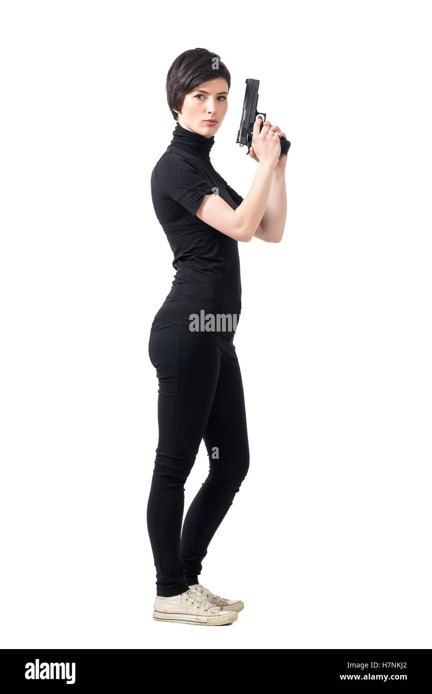Seitenansicht des bewaffneten taffe Frau mit Pistole Blick in die Kamera. Ganzkörper-Länge-Porträt über weiße Studio-Hintergrund isoliert. Stockfoto