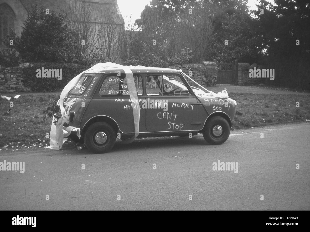 1960er-Jahren, historische, ein verheiratetes Paar Mini Auto geschmückt mit Bändern und Spaß Parolen auf der Hochzeit außerhalb der Kirche. Stockfoto