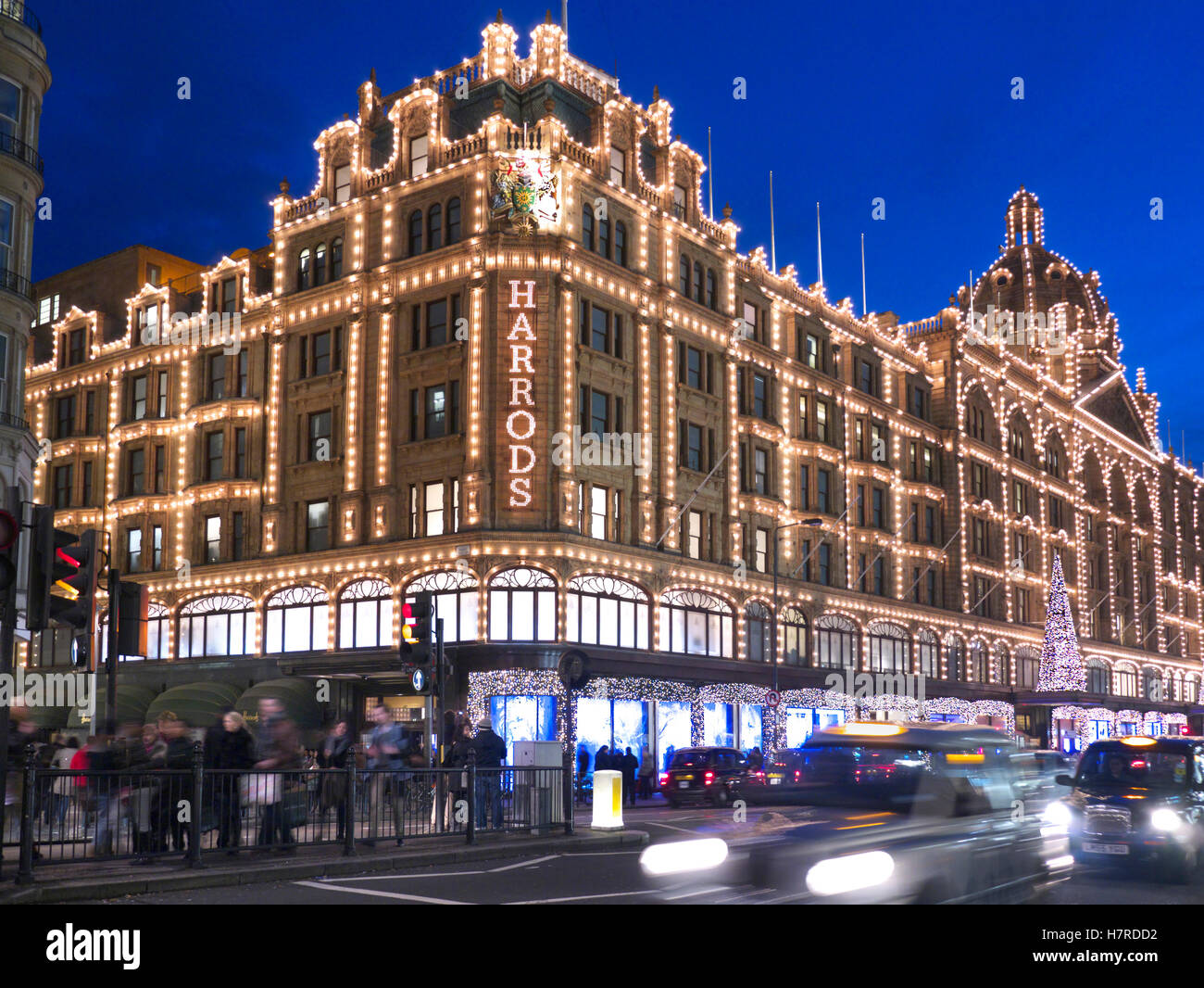 LONDON CHRISTMAS SHOPPING Kaufhaus Harrods in der Dämmerung mit Weihnachtsbeleuchtung Shopper und verschwommenes Taxis mieten Knightsbridge London SW1 Stockfoto
