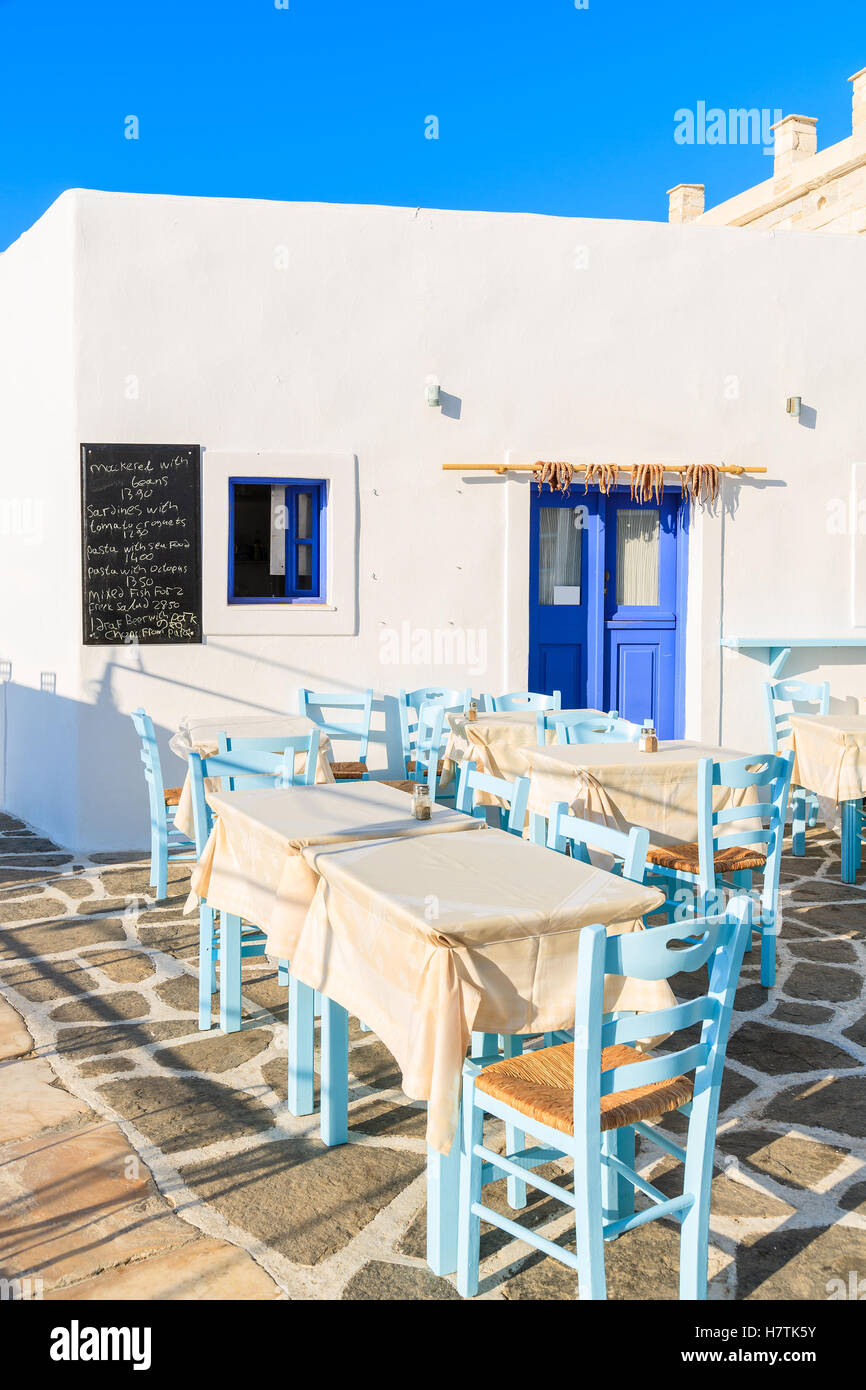Tische mit Stühlen in griechische Taverne in Naoussa Hafen, Insel Paros, Griechenland. Menü-Tafel an der Wand zeigt Gericht Namen mit Preisen. Stockfoto