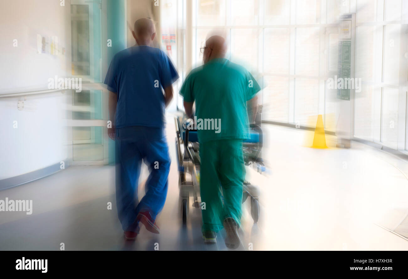 Arzt und Chirurg schieben ein Patient auf einem Krankenhaus-Bett-Wagen durch die Notaufnahme eines Krankenhauses in UK. Stockfoto