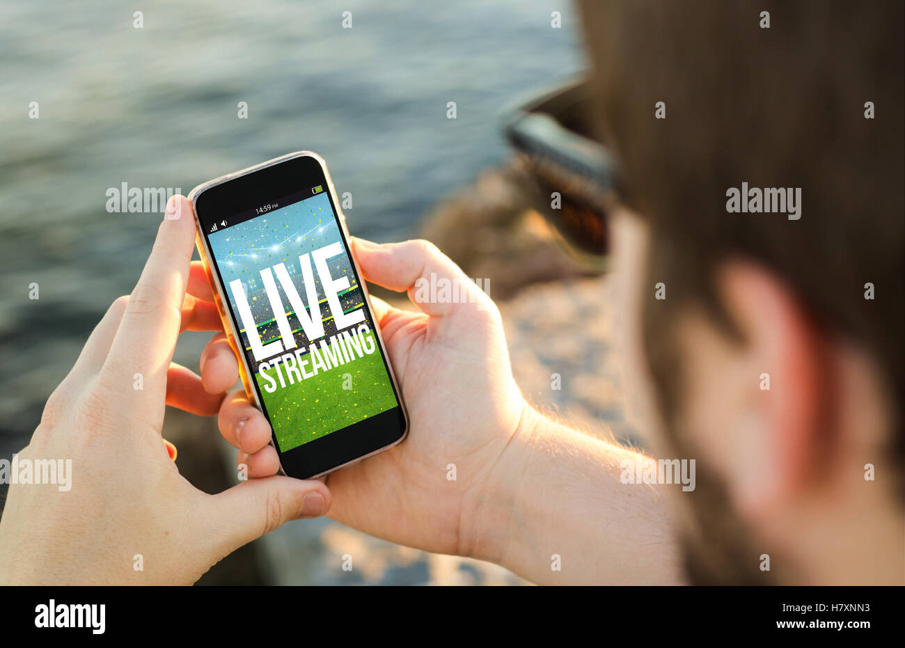 Mann an der Küste mit seinem Smartphone Wih live Streaming-Sport-Event. Alle Bildschirm-Grafiken bestehen. Stockfoto