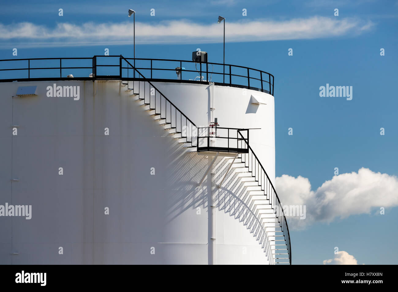 Nahaufnahme eines Teils der einen großen weißen Speichertank mit schwarzem Eisentreppe wirft einen Schatten auf den Tank und den blauen Himmel und die Wolken; Alberta, Kanada Stockfoto