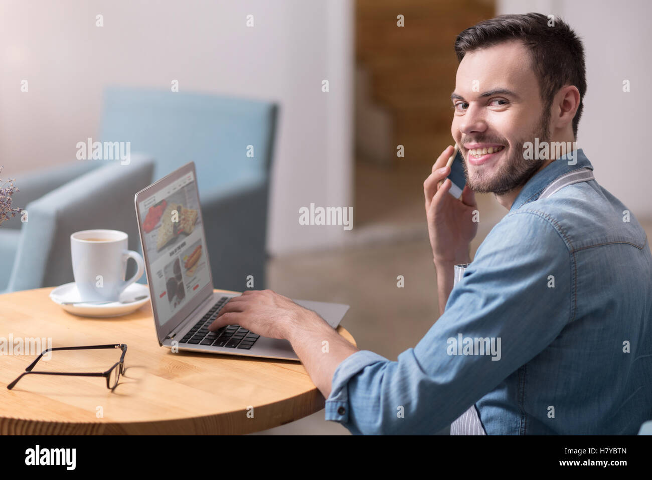 Amüsiert lächelnden Mann mit Laptop und am Handy sprechen. Stockfoto