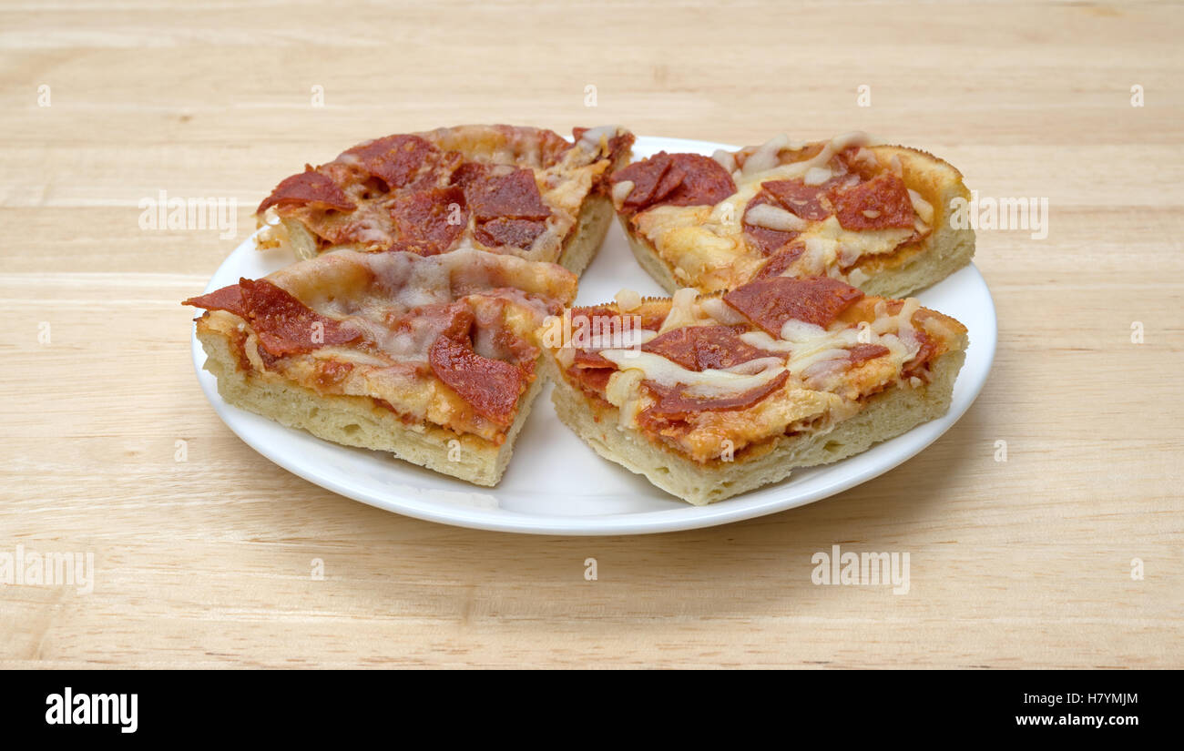 Einige Mikrowelle persönliche Größe Peperoni Pizza Scheiben isoliert auf einem weißen Teller oben auf einem Holztisch. Stockfoto