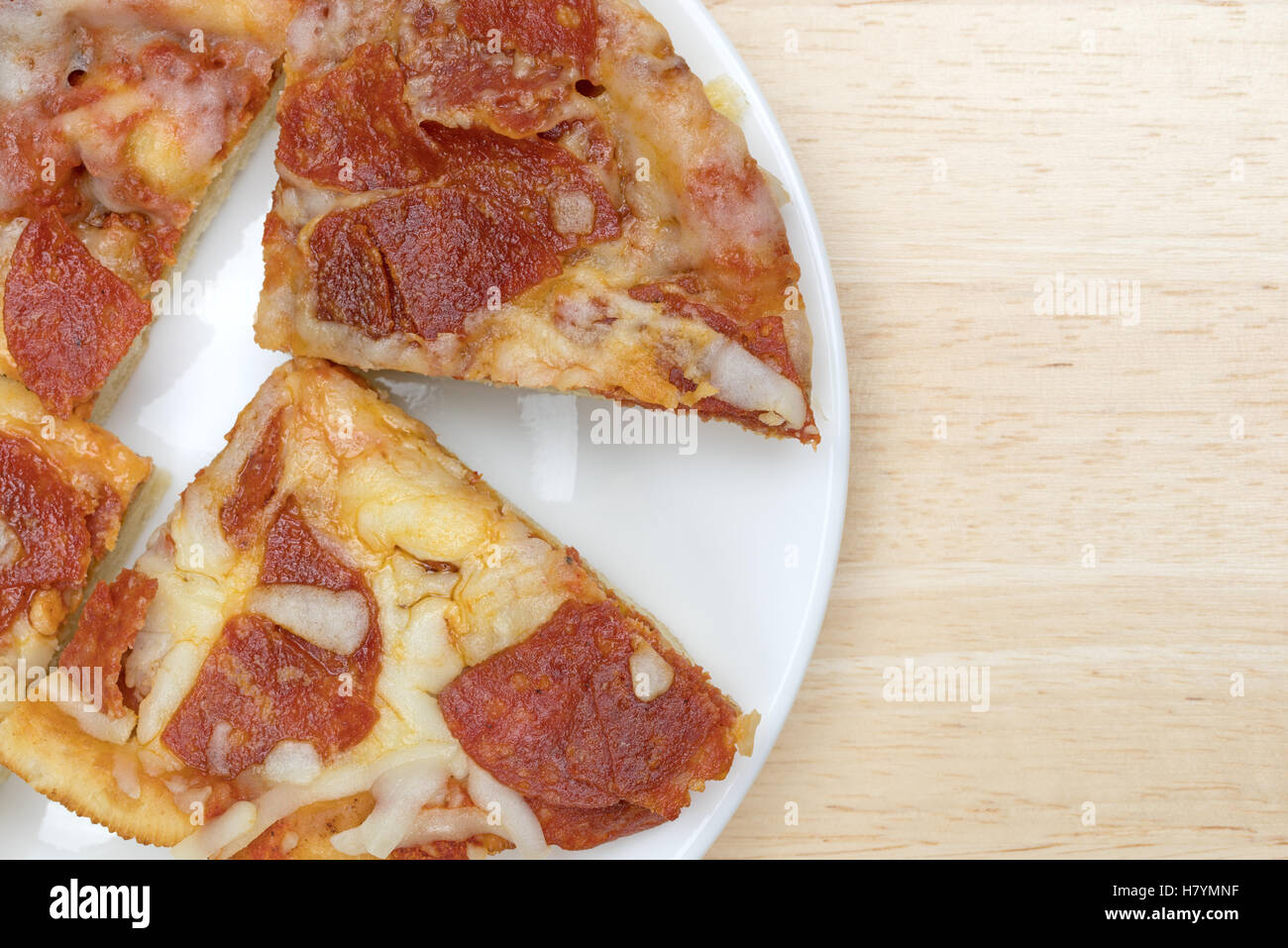 Enge Draufsicht von mehreren Mikrowelle persönliche Größe Peperoni Pizza Scheiben isoliert auf einem weißen Teller oben auf einem Holztisch. Stockfoto