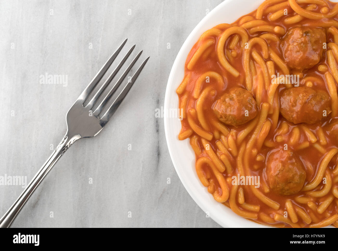 Draufsicht auf eine Portion Spaghetti und Fleischbällchen auf einem weißen Teller mit einer Gabel auf der Seite oben auf einer grauen Marmor Tischplatte. Stockfoto