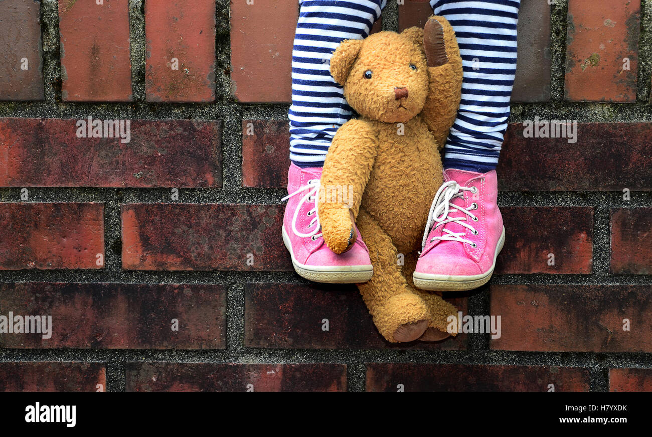 Teddy eingespannt zwischen Beinen, Kind sitzt auf Wand, Detail, Deutschland Stockfoto