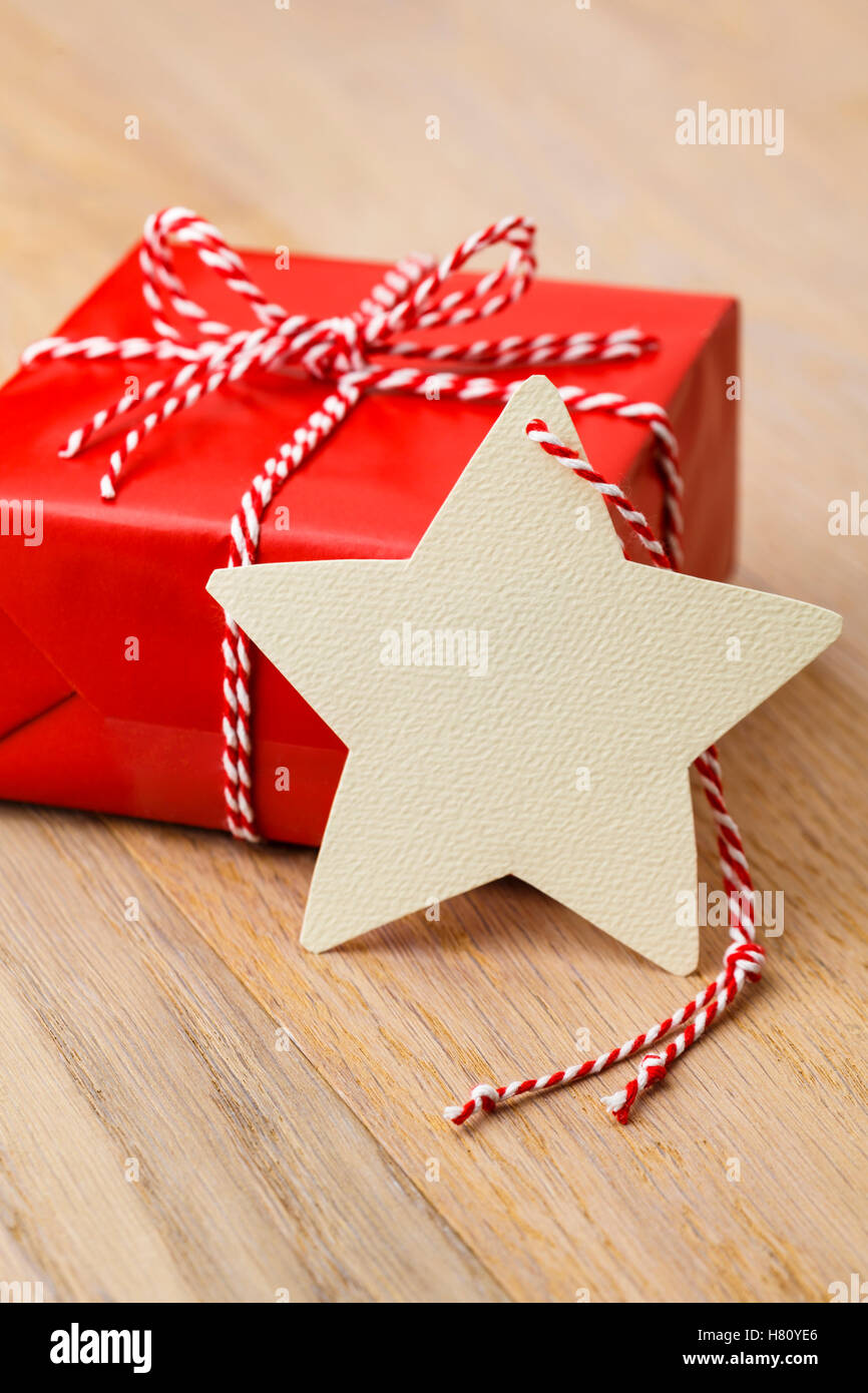 Einfache, klassische rote Weihnachtsgeschenk mit handgefertigten leer Geschenkanhänger auf rustikalen Holz vertikale Hintergrund präsent. Stockfoto