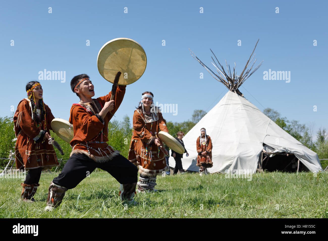 Männer und Frauen tanzen mit einem Tamburin auf dem Rasen auf einem Hintergrund Yaranga. Feier des Tages der erste Fisch: Feier Ureinwohner Kamtschatkas Stockfoto
