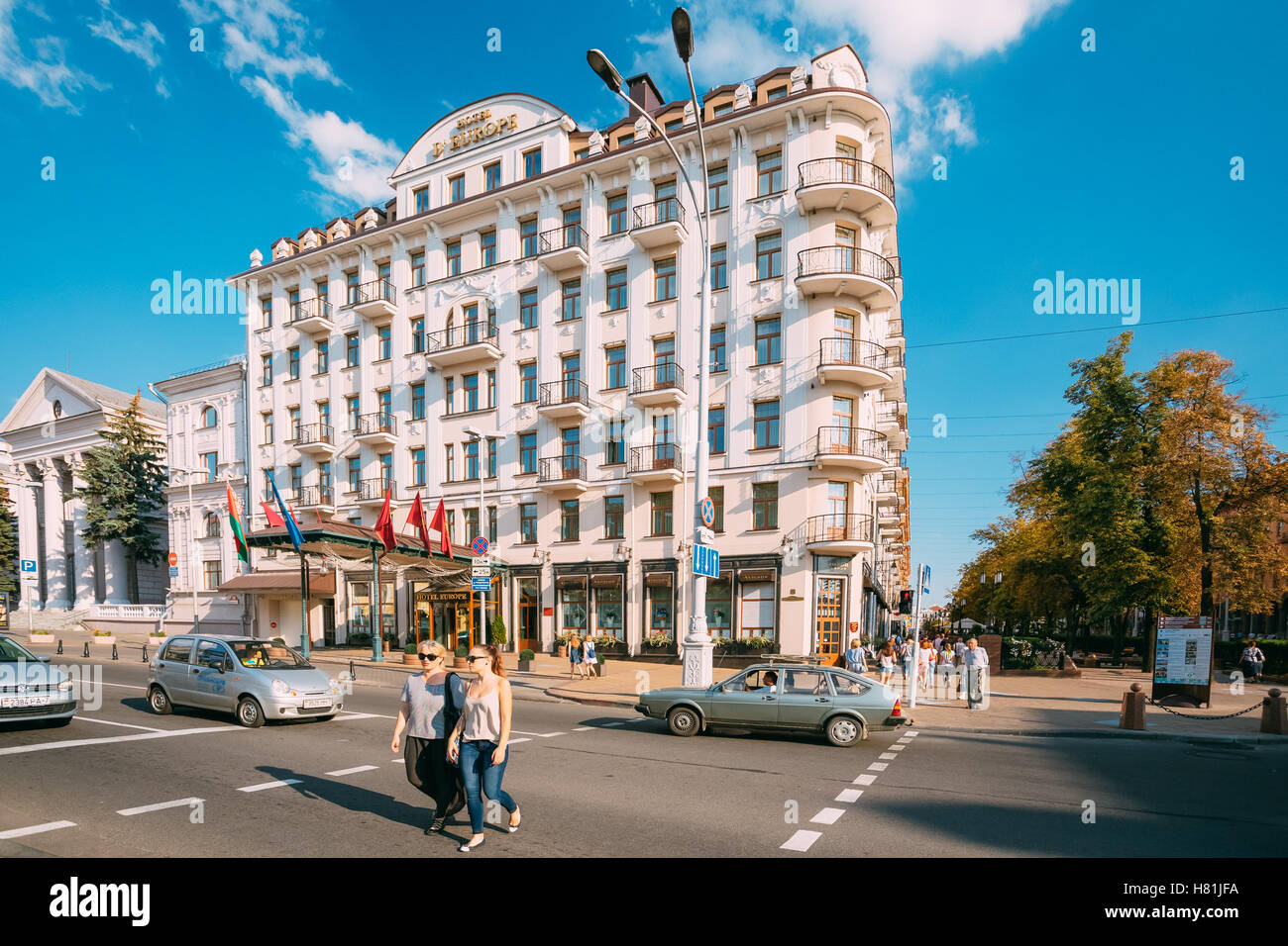 Minsk, Weißrussland. Zwei Frauen In Sonnenbrille, Casual tragen Kreuzung International Street am Zebrastreifen. Fassade des Europa Hotelgebäude Stockfoto