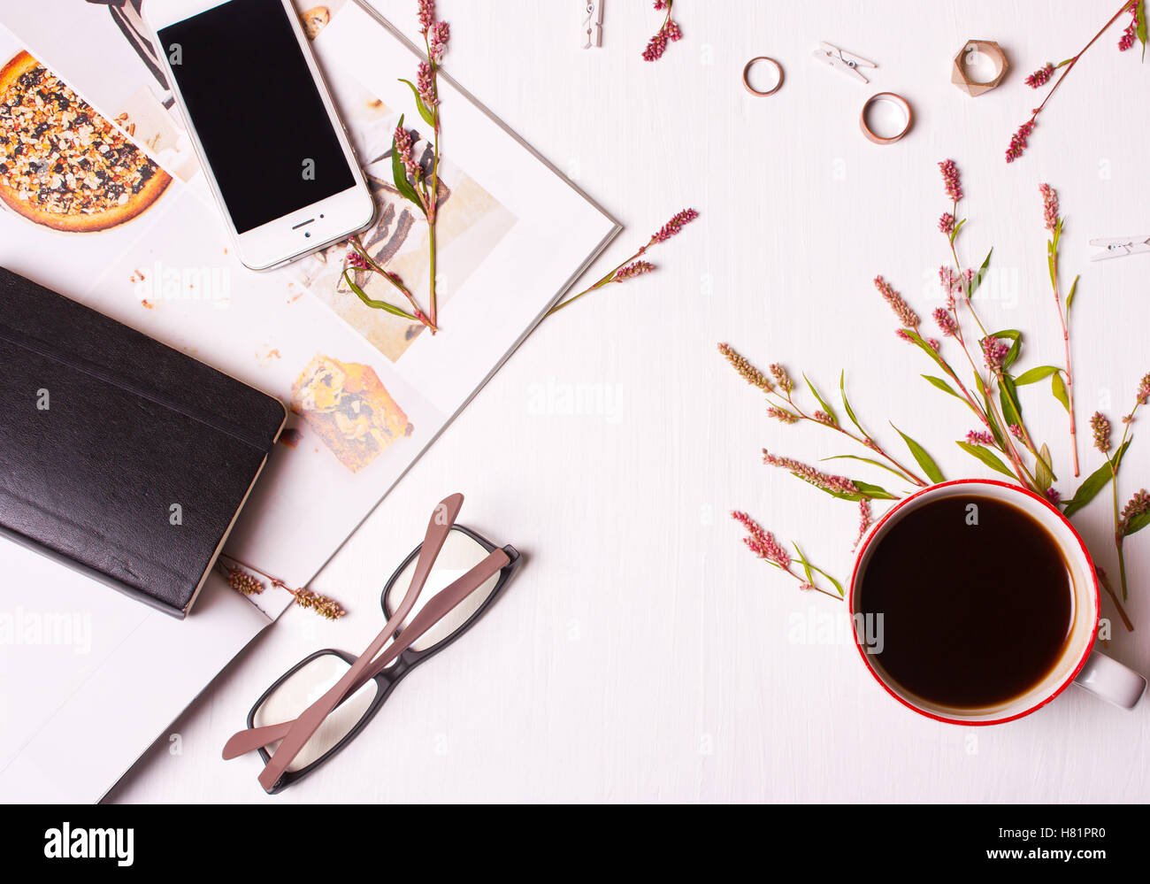 Draufsicht der Designertisch, eine Frau mit einer Tasse Kaffee, Magazin, Handy, Brillen, Ringe, Blumen und ein Notizblock. Arbeitsbereich. Stockfoto