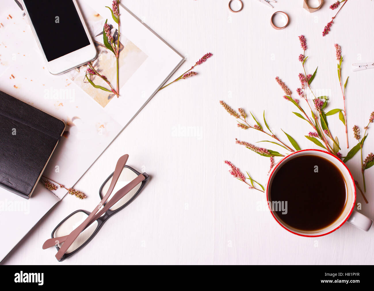 Draufsicht der Designertisch, eine Frau mit einer Tasse Kaffee, Magazin, Handy, Brillen, Ringe, Blumen und ein Notizblock. Arbeitsbereich Stockfoto