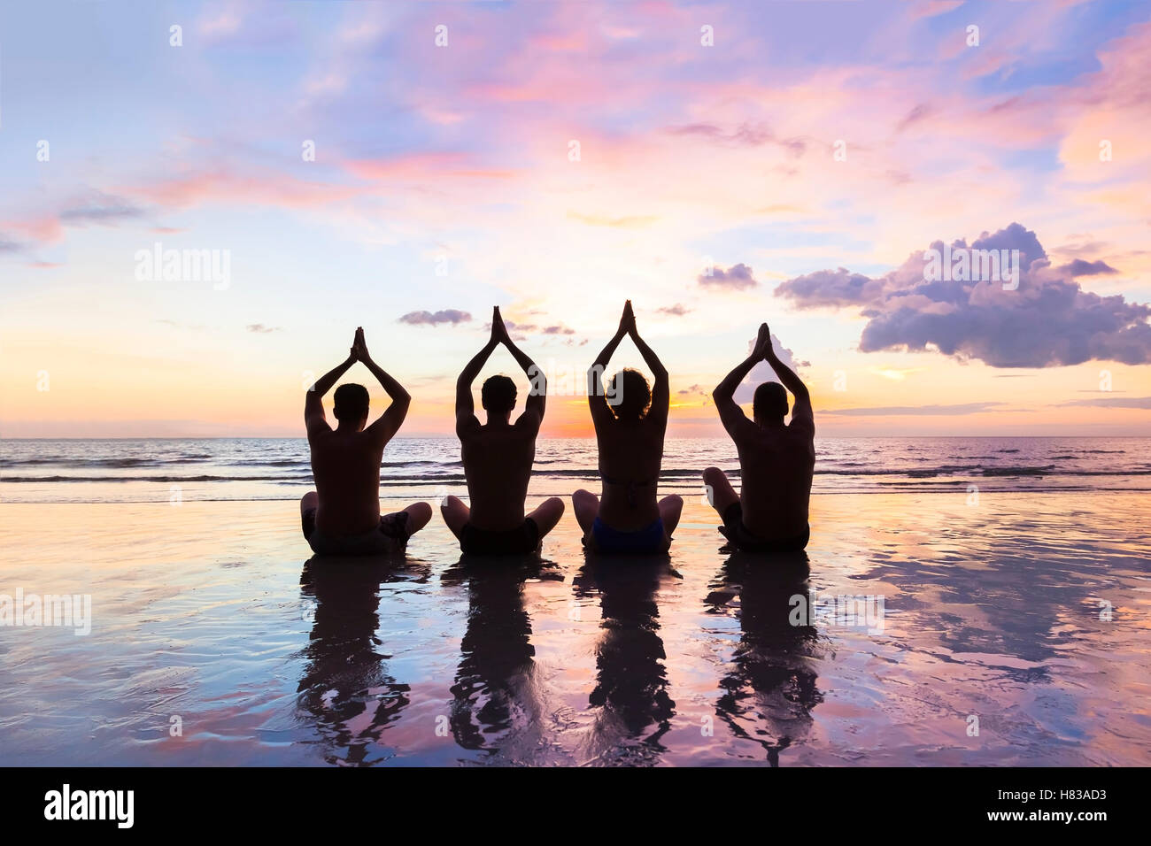 Gruppe von vier Personen üben Meditation und Yoga am Strand bei Sonnenuntergang - Konzept über Freunde, Familie, Harmonie und gesund Stockfoto