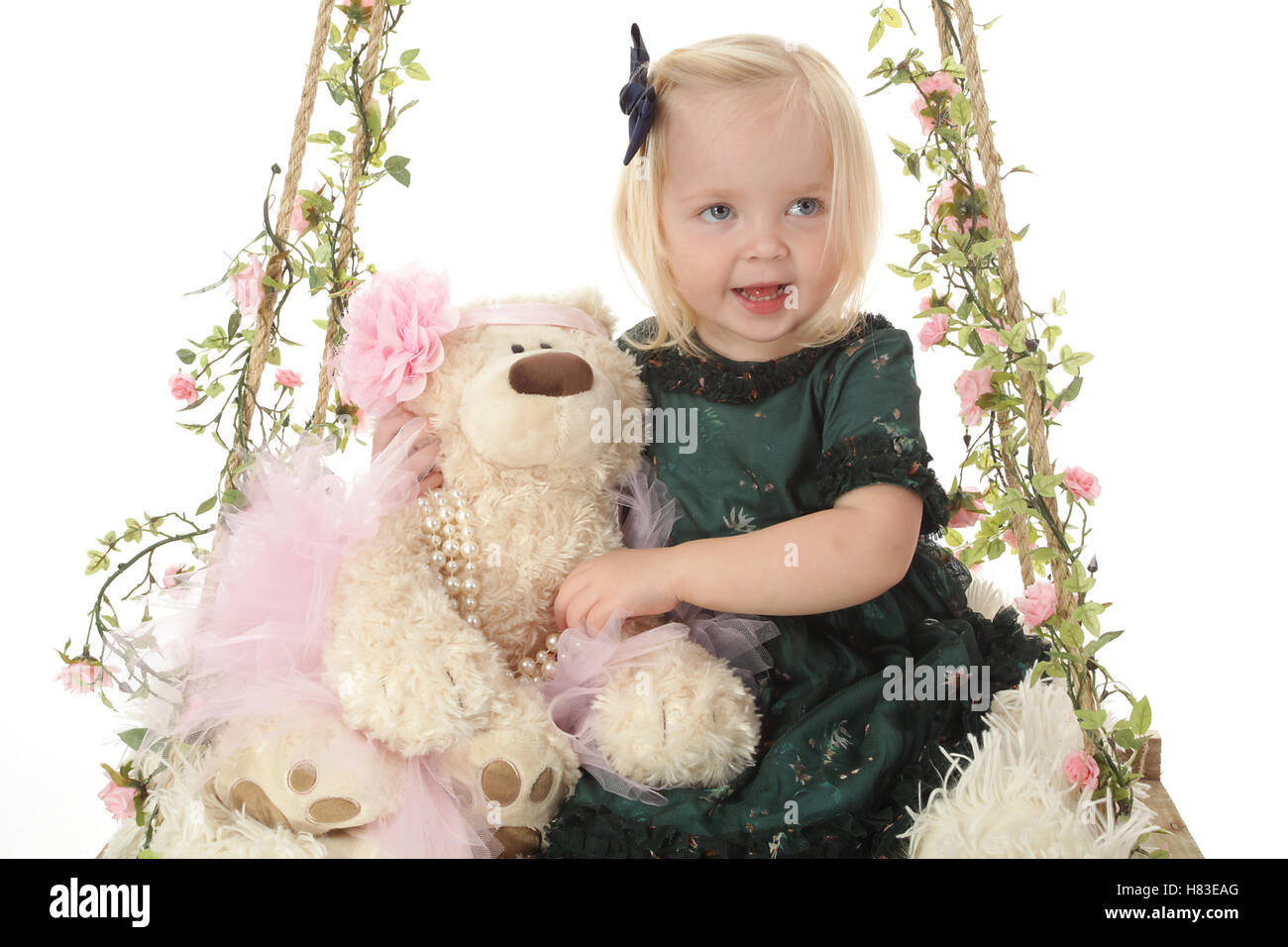 glückliches kleine Mädchen auf Fotostudio swing mit Blumen und teddy Stockfoto