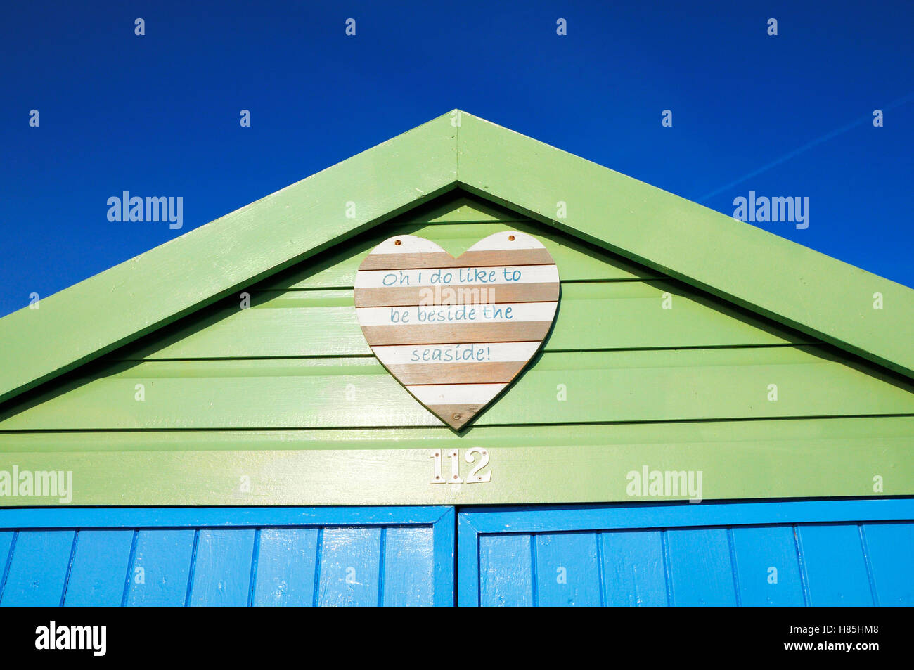 Frisch gestrichene Strandhütte mit einer fröhlichen Herz aus Holz-Plakette, die Anzeige der Songtexte "Oh ich mag neben dem Meer sein!" Stockfoto