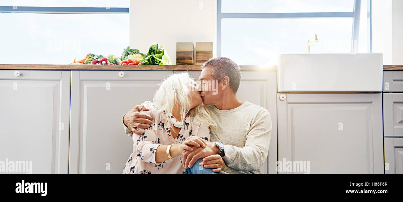 Porträt von zwei älteren Ehepaar sitzt auf einem Küchenboden, umarmen und küssen Stockfoto