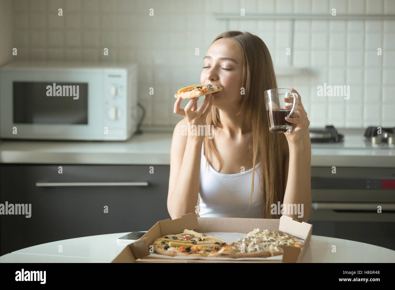 Porträt einer jungen Frau, die auf der Küche Pizza essen Stockfoto