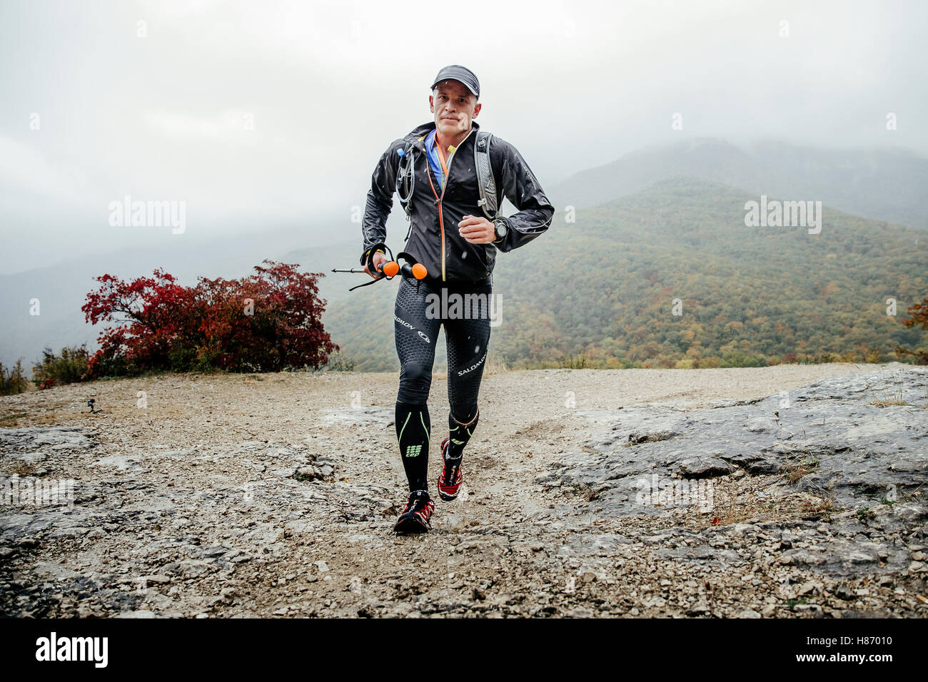 Läufer laufen im Regen auf einem Bergweg mit walking-Stöcken während Crimea Mountain Marathon Männer mittleren Alters Stockfoto
