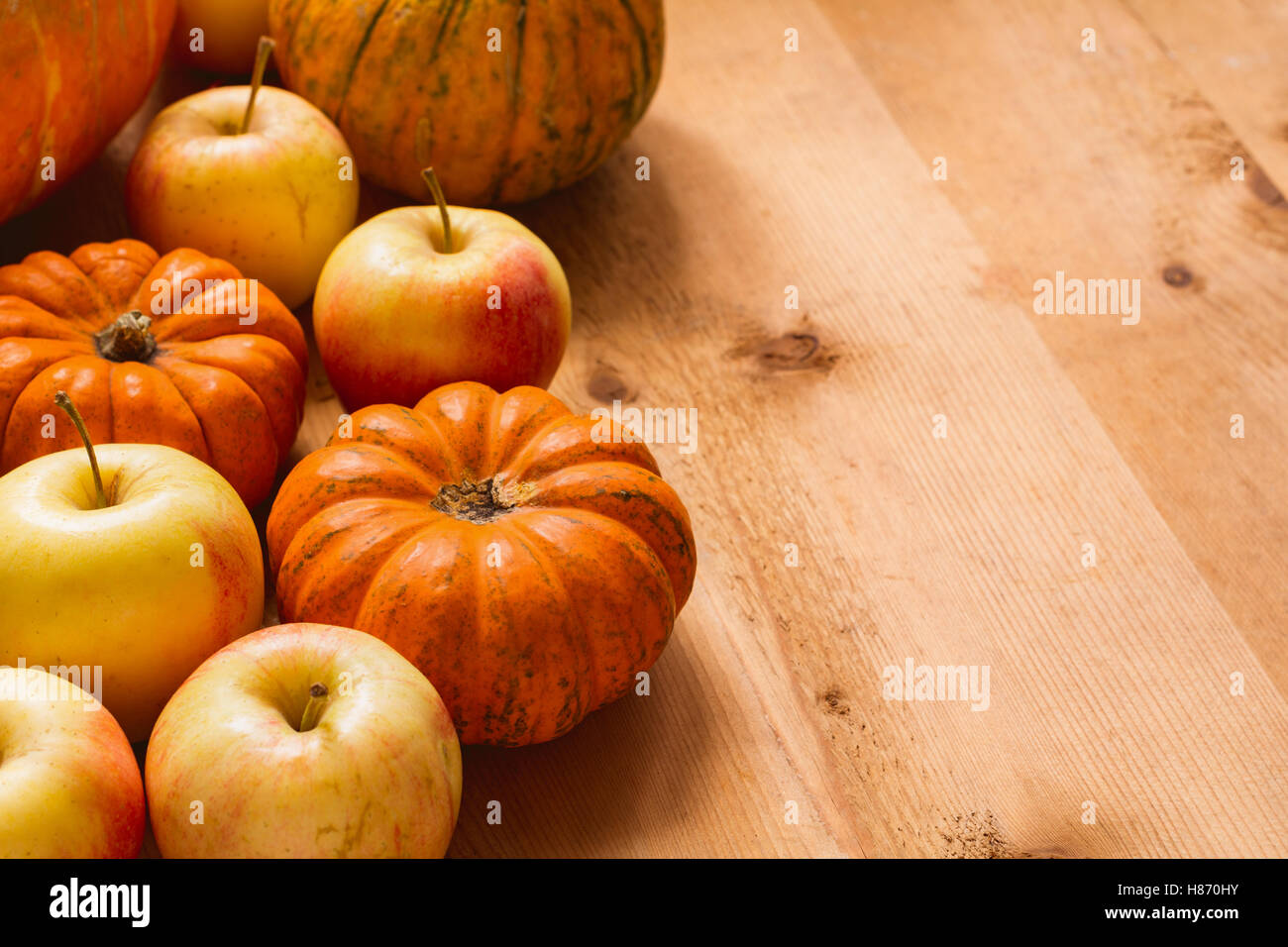 Kleine Kürbisse und Äpfel auf Holztisch mit textfreiraum für Text. Herbsternte, Lebensmittelzutaten zum Erntedankfest. Horiz Stockfoto