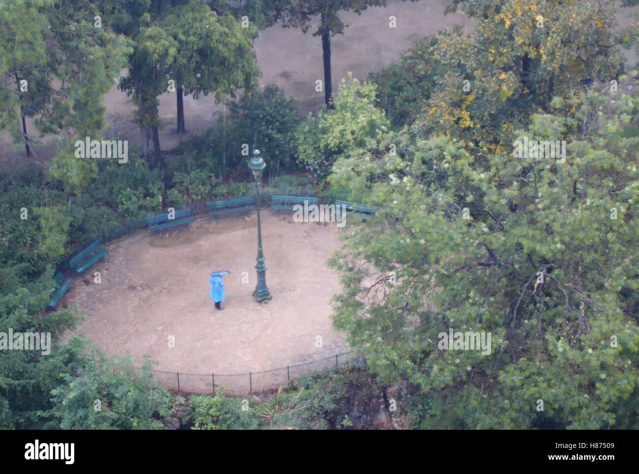 Person mit Regenschirm wartet im Regen unter dem Eiffelturm Garten, Paris Frankreich. Stockfoto