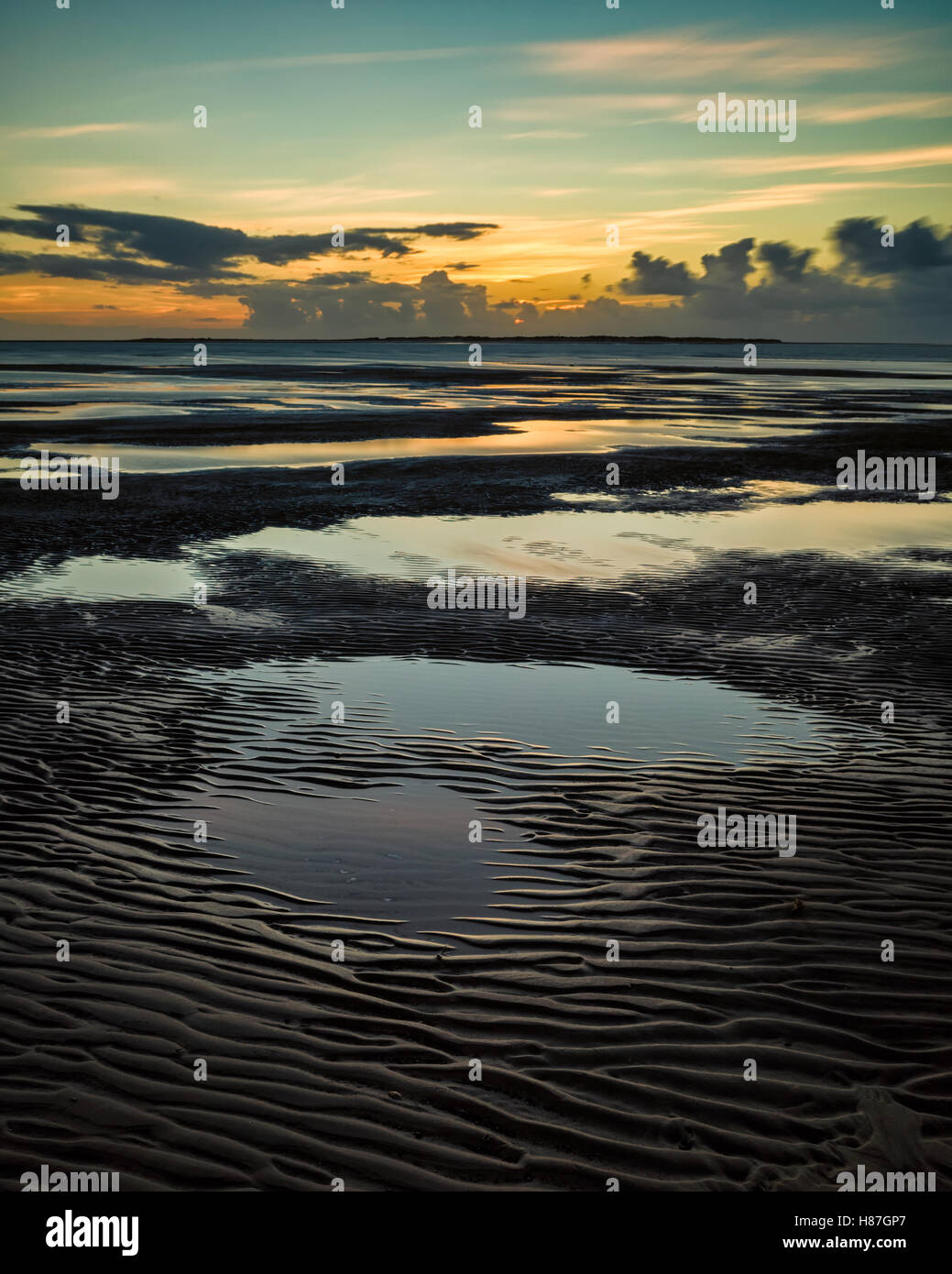 Flinthorndünen, Langeoog. Deutschland. Deutschland. Ein Blick von der Buche bei Ebbe mit dem Sonnenuntergang über der benachbarten Insel Baltrum. Fotografiert zehn Minuten nach Sonnenuntergang etwas warmes Licht auf dem Wasser, während das Meer rund um die blaufärbung Himmel spiegelt wider. Tiefe Muster in der Sandstrand lassen flache Becken mit Wasser, die auch sind voll von Reflexionen. Stockfoto