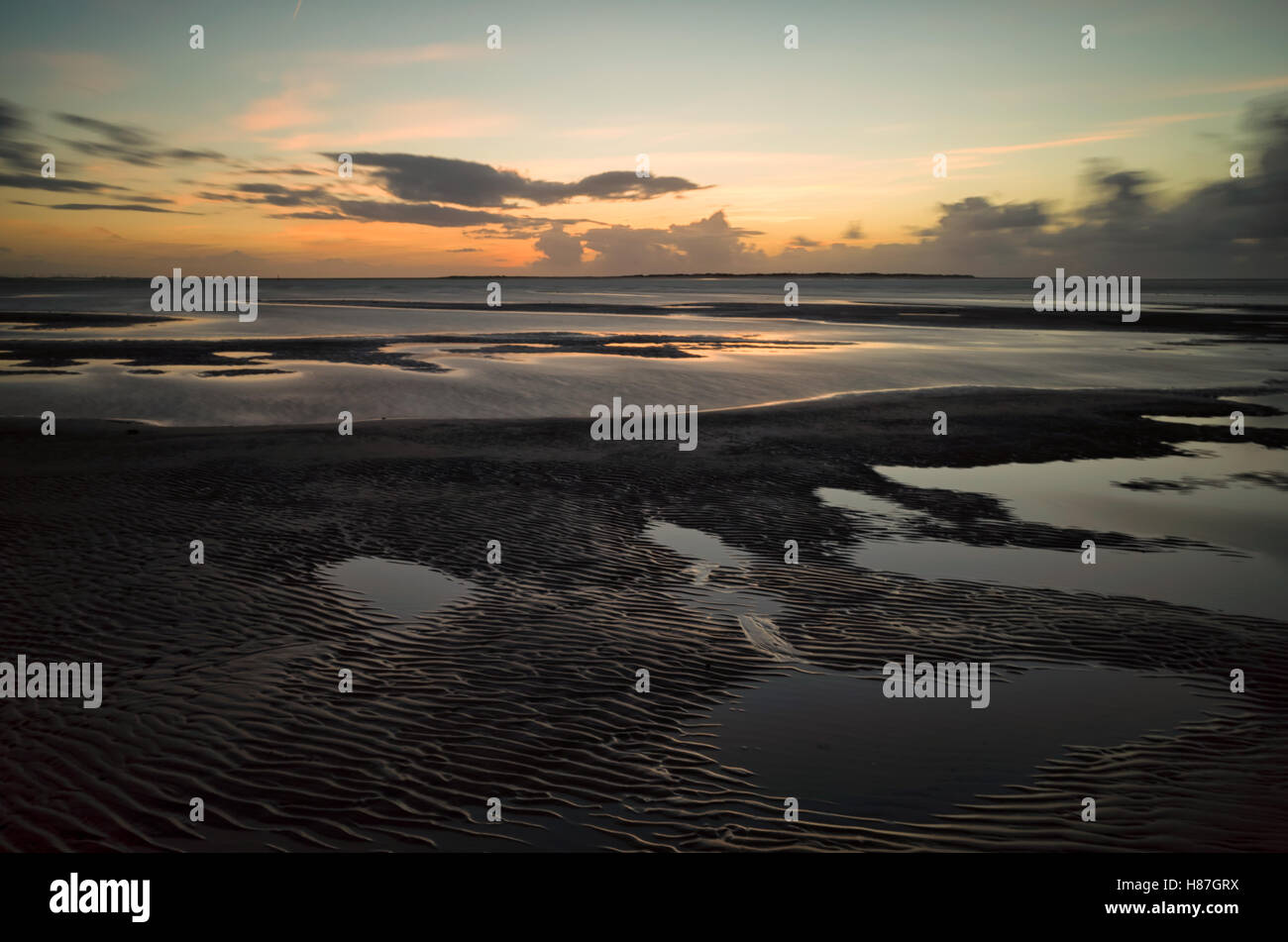 Flinthorndünen, Langeoog. Deutschland. Deutschland. Ein Blick von der Buche bei Ebbe mit dem Sonnenuntergang über der benachbarten Insel Baltrum. 20 Minuten nach Sonnenuntergang fotografiert einige warme Licht auf dem Wasser, während das Meer rund um die blaufärbung Himmel spiegelt wider. Tiefe Muster in der Sandstrand lassen flache Becken mit Wasser, die auch sind voll von Reflexionen. Stockfoto