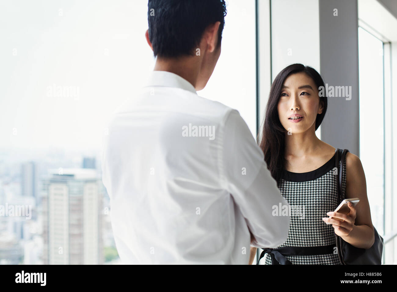 Ein Geschäftsmann und Geschäftsfrau stehend reden durch ein großes Fenster mit Blick auf eine Stadt Stockfoto