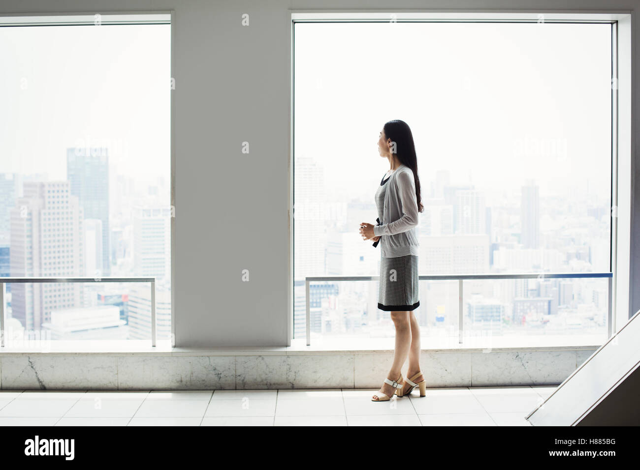 Eine Business-Frau in einem Kleid von einem Fenster mit Blick auf eine Stadt Stockfoto