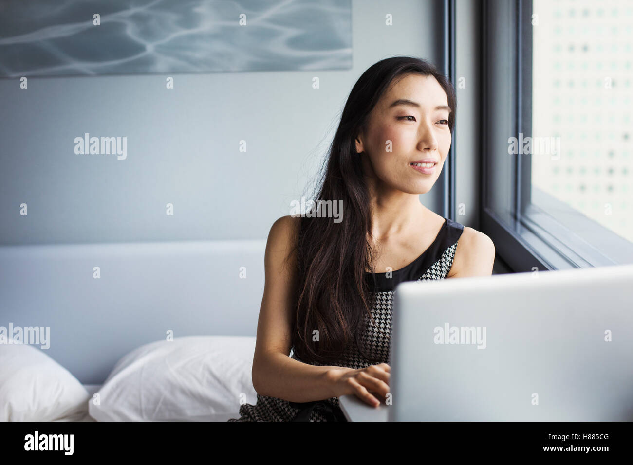 Eine Geschäftsfrau gekleidet, sitzt auf ihrem Bett mit einem Laptop. Stockfoto