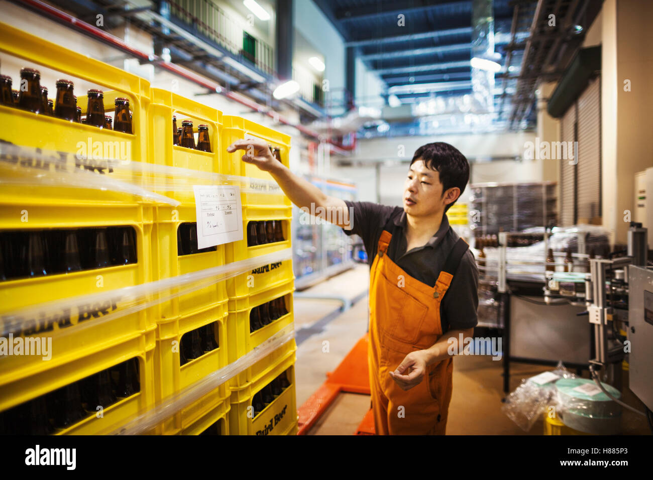 Arbeiter Kennzeichnung gelbe Kunststoff-Kisten mit Bierflaschen in einer Brauerei. Stockfoto